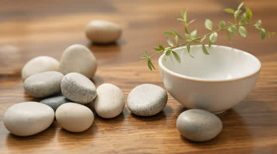 Smooth stones, a pale ceramic bowl and a sprig of greenery on walnut