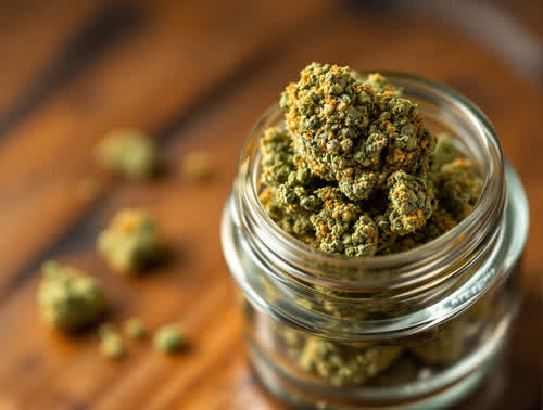 Northern Lights hemp flower in a clear glass jar on walnut